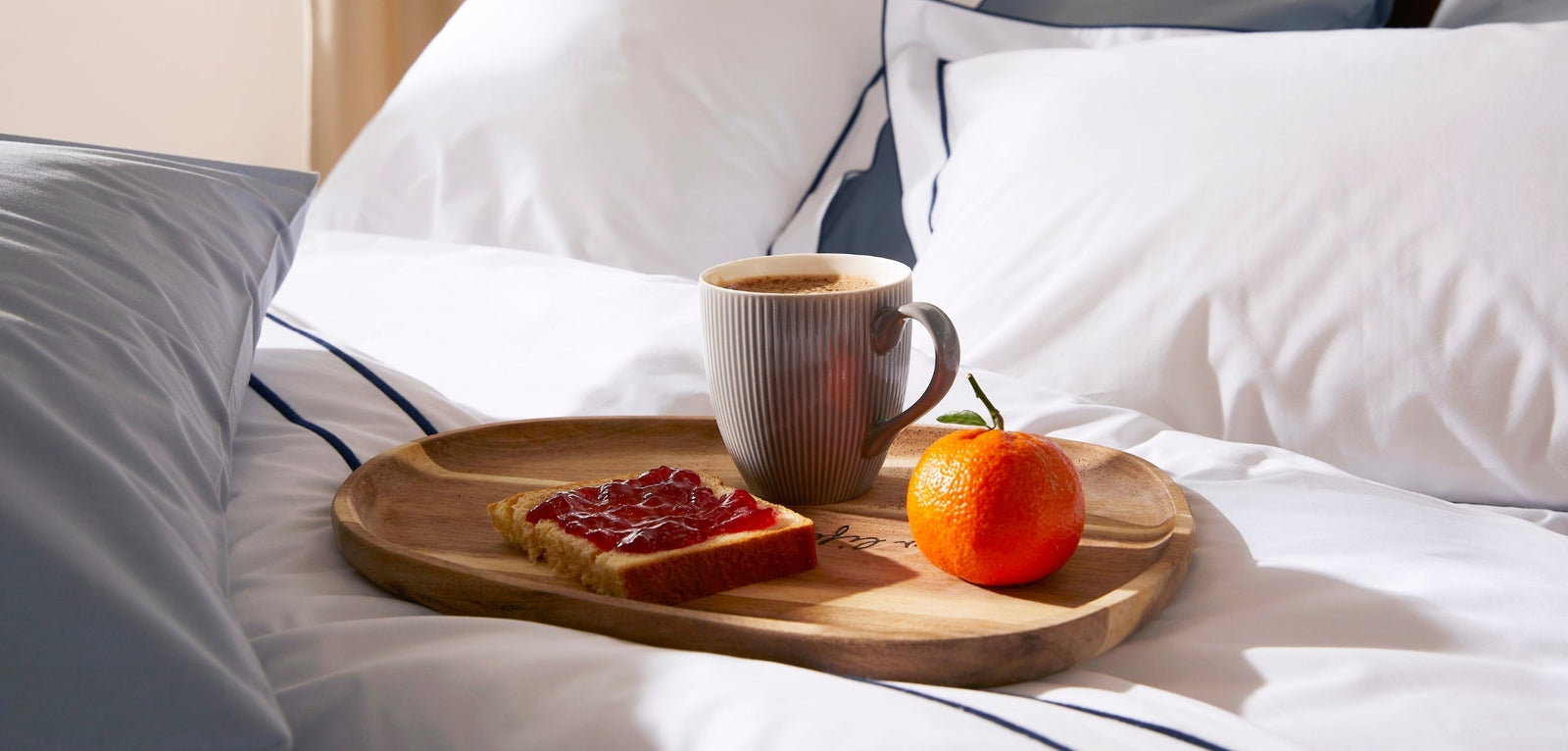 Un plateau en bois posé sur un lit blanc, contenant une tasse de café, une tartine à la confiture et une clémentine, illustrant un petit-déjeuner sain au réveil.
