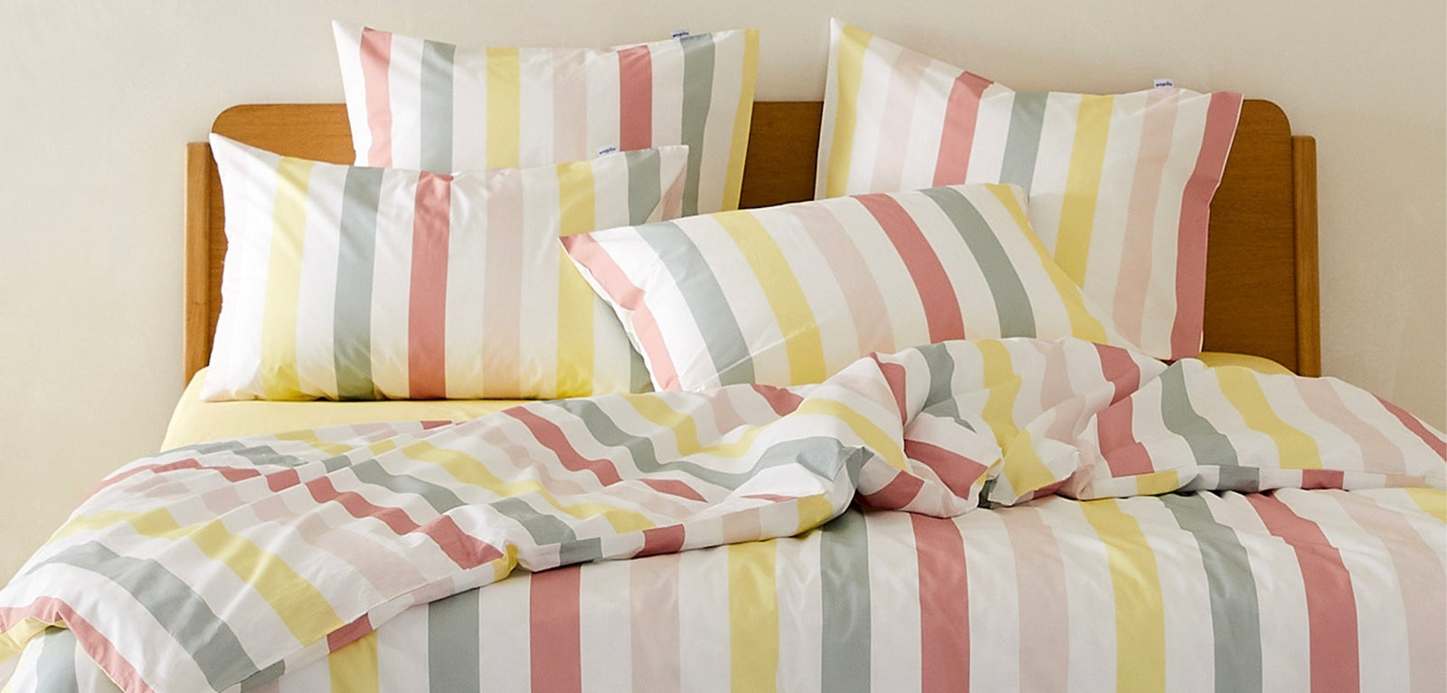 Lit double avec parure de lit à rayures pastel (jaune, rose, vert et beige), comprenant housse de couette et taies d’oreiller assorties, disposé dans une chambre lumineuse au mobilier en bois clair.