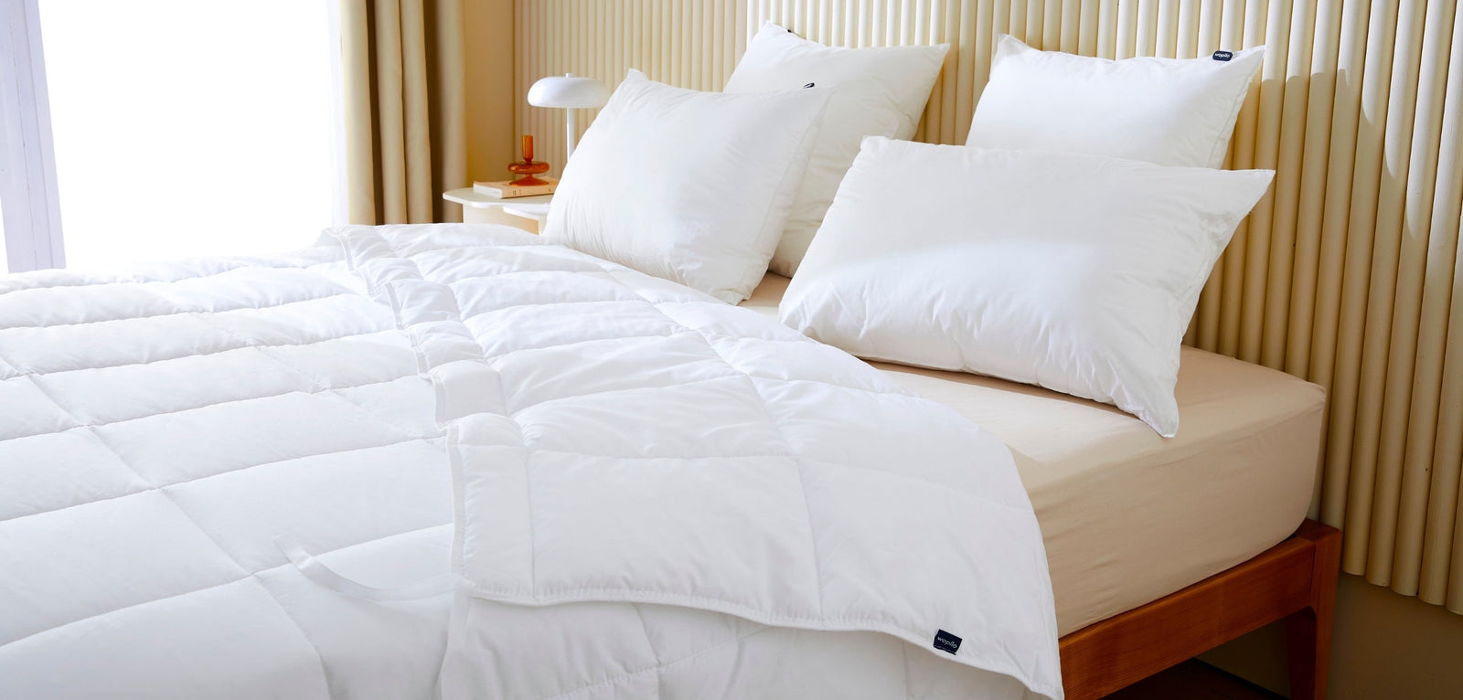 Un lit bien fait avec une couette blanche piquée et plusieurs oreillers blancs volumineux, mettant en avant un ensemble de literie propre, confortable et accueillant.