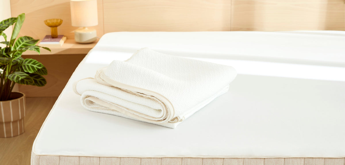 Matelas blanc avec sa housse plié dessus, dans une chambre lumineuse et chaleureuse