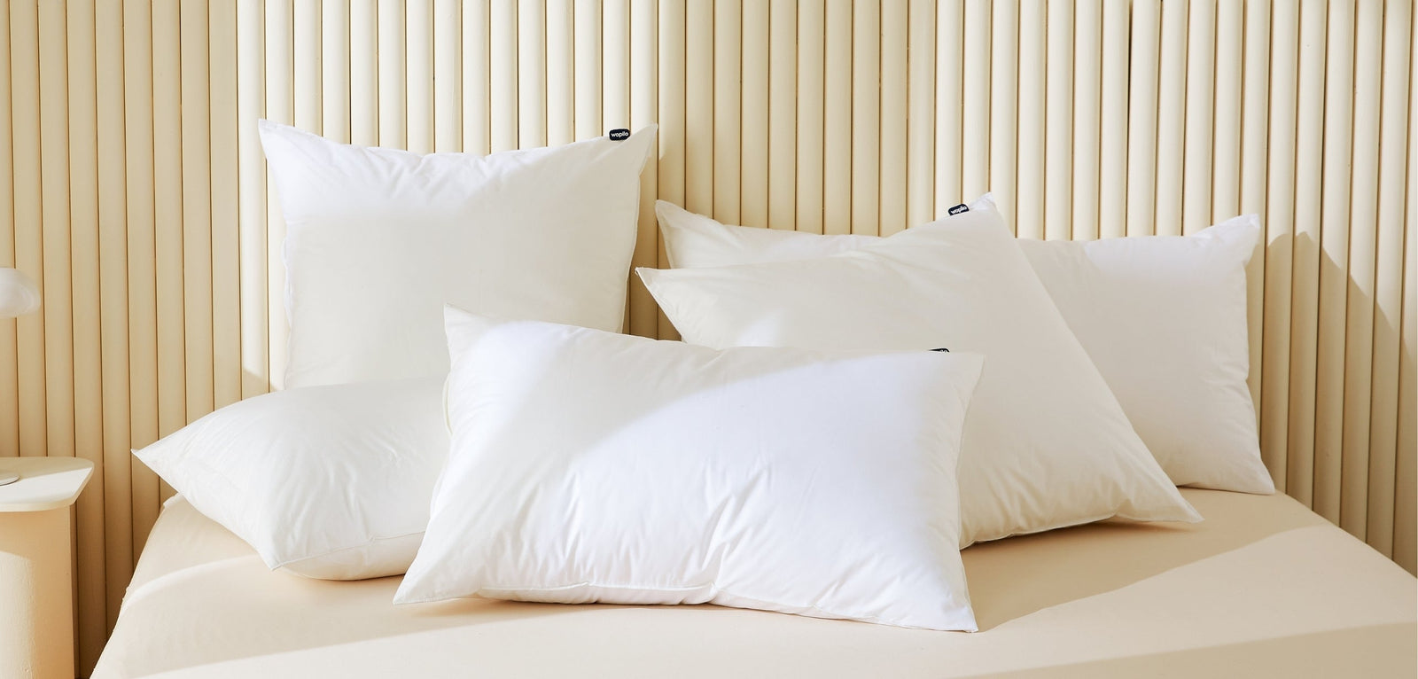L'ensemble des oreillers Wopilo, empilés sur un lit devant une tête de lit design en lattes verticales beiges.